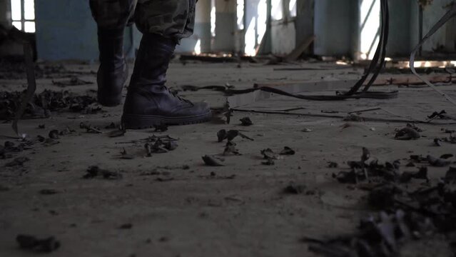A stalker soldier in army boots walks through an abandoned factory, close-up of his legs. Post-apocalyptic concept