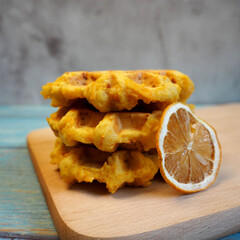 three pumpkin gluten-free Belgian waffles lie on a wooden board next to a dried orange slice. breakfast. snack.  sweets