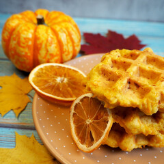 three pumpkin gluten-free Belgian waffles lie on a brown plate next to two dried orange slices. breakfast. snack. healthy sweets