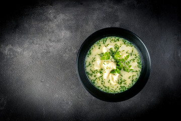 Cauliflower cream soup garnished with chives, chervil and marjoram, on a dark grey stone background