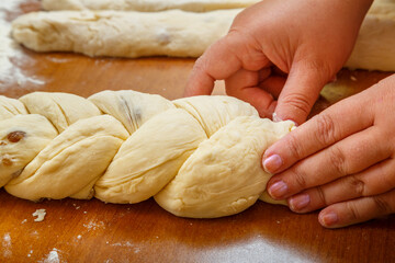 The hands of a Jewish woman weave challah with a pigtail for a festive meal.
