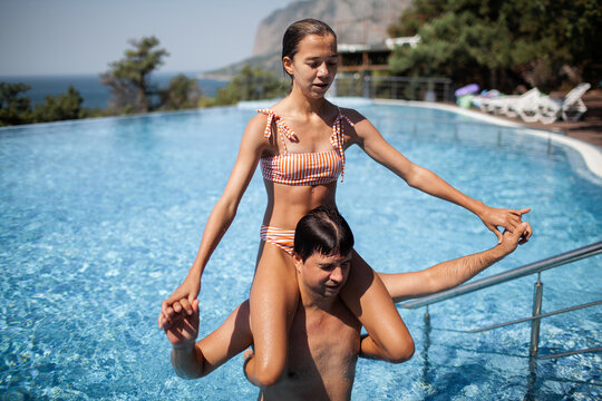 The guy is holding a teenager girl on his shoulders in the pool, people having fun rest together