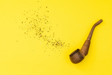 Wooden smoking pipe with tobacco on a yellow background, smoking harms