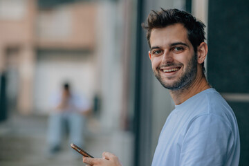 attractive young man with beard smiling on the street with mobile phone