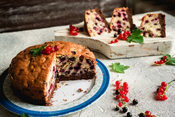 pieces of sliced berry fruit cake with black and red currants on a gray concrete background 1