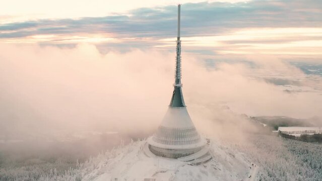 Dense fog surrounds Jested tower with large spire on winter day. Modern architecture on high forestry mountain top in Czech Republic aerial view
