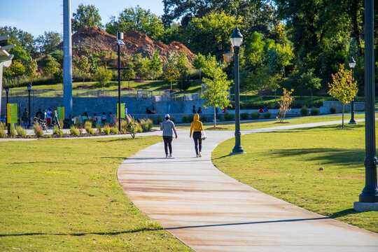 two African American women walking along a smooth footpath at Rodney Cook Sr. Park in Historic Vine City surrounded by lush green trees, grass and plants in Atlanta Georgia USA