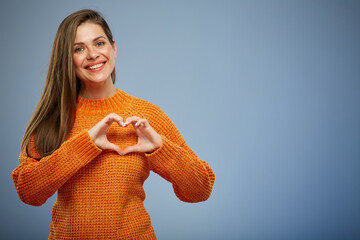 Smiling woman in warm orange sweater making heart with finger. - 535639517