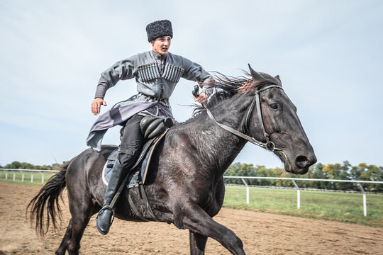 Cossack man in a national costume is galloping rapidly on a black horse around the hippodrome