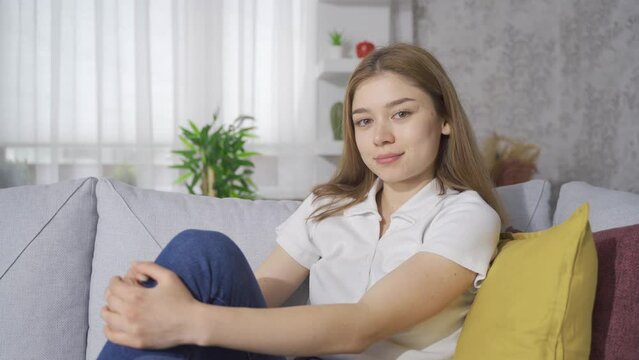 Young woman sitting on sofa looking at camera and smiling.
Young woman sitting on sofa at home smiling looking at camera.
