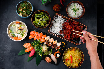 Set of Chinese dishes on table, hands holding chopsticks sweet and sour chicken, noodles, rice