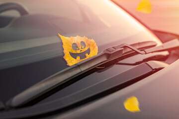 Cheerful yellow leaf with emotion, on the windshield of the car under the brush. Concept of warm...