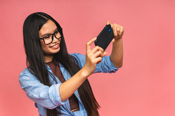 Happy Asian portrait beautiful cute young woman teen smiling excited typing text message on smart mobile phone enjoys online communication isolated on pink background with copy space.
