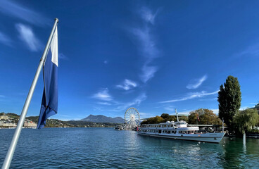 Blick über den Vierwaldstätter See mit weiß blauer Fahne im Vordergrund und einem Ausflugs...