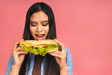 Young beautiful asian japanese chinese woman eating sandwich or big burger with satisfaction. Girl enjoys tasty hamburger takeaway, diet concept, standing isolated over pink background. - Powered by Adobe