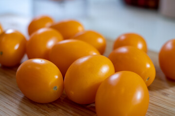 bright yellow delicious tomatoes on a wooden board on a white table with a blurred kitchen in the background