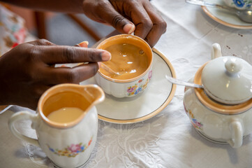 Close up of young woman's hands preparing and drinking a coffee with milk and sugar using a vintage porcelain cup with flowers pattern