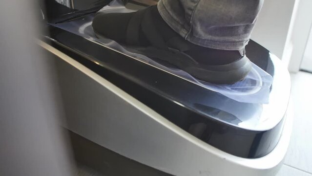 Close-up of a male foot in street shoes put in an automatic shrink shoe laminator at the entrance to a medical clinic. During the quarantine period, it is necessary to laminate shoes for safety