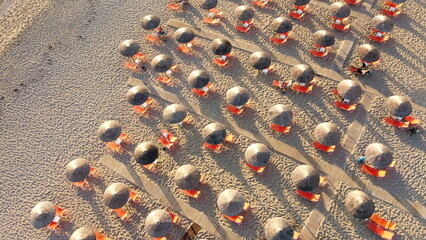 Aerial view of rows of cane umbrellas and sunbeds on a sandy Mediterranean beach