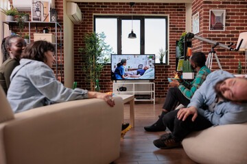 Men and women drinking beer and watching drama movie on tv, having fun together at gathering with drinks and film on television channel program. People looking at reality show content.
