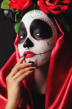 catrina in red dress in celebration of the day of the dead with hand gesture and expression of security, dark background and sugar skull makeup