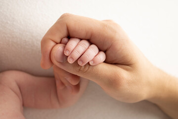 The hand of a sleeping newborn in the hand of parents, mother and father close-up. Tiny fingers of a newborn. 