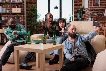 Young people having fun with photos taken on smartphone camera, creating memories together at social gathering with beer and snacks. Friends taking pictures drinking and relaxing.