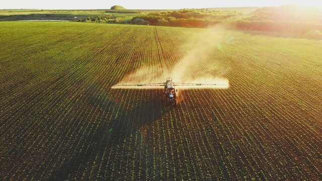 Aerial view of working farming tractor spraying on field with sprayer water or herbicides and pesticides against diseases and insects. Nature landscape of rivers, reservoirs. Agricultural industry.