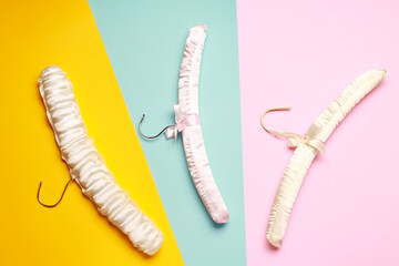 Top view flat lay different empty silk clothes hangers at blue yellow pink background. Sale store design, shopping concept.  