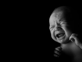 Baby boy crying, studio light used on a black background.