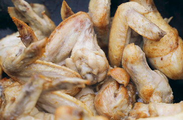 The cook prepares chicken - legs and wings in a cauldron in the open air.