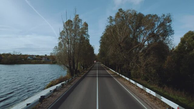 Aerial photography of a beautiful highway along the lake, the road under the branches of trees