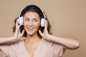 woman in white headphones on a beige background dances and sings to music. a beautiful European woman with curly hair listens to her favorite songs online or on the radio, podcast. audio content for