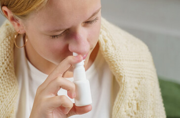 A girl with a cold treats a runny nose with a nasal spray.