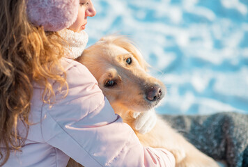 Portrait of young beautiful woman in pink headphones with curly hair sitting and hugging her golden retriever dog. Happiness and friendship. pet and woman. Winter landscape on the laying of the river 
