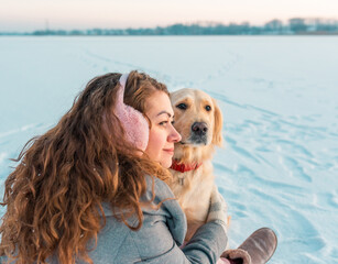 Smiling woman hugging her pet dog golden retriever near face. Golden retriever playing with a woman walking outdoors winter day, warm clothing. love and care for the pet.