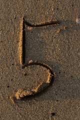 Fototapeta na wymiar The number five is drawn in the sand. Educational spelling.