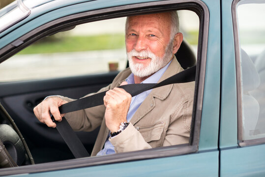 Smiling senior man putting seat belt before driving car