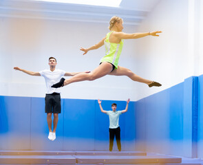 Fototapeta premium View through yellow safety net of athletic young woman training jumping movements in indoor trampolines center