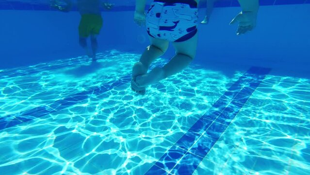 Leisure time activities concept. Underwater shot of a caucasian boy swimming around in turquoise swimming pool. Summer holidays. High quality 4k footage