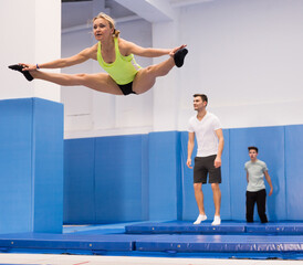 Smiling female gymnast jumping and bouncing on trampoline during workout in modern fitness center