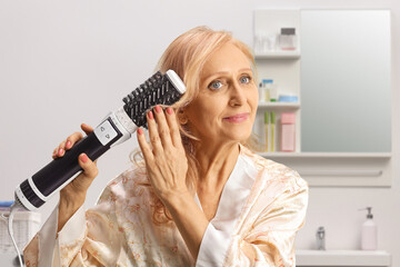 Beautiful mature woman in a bathrobe using a hot air hair brush