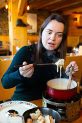 Portrait of young adult woman eating cheese fondue at restaurant