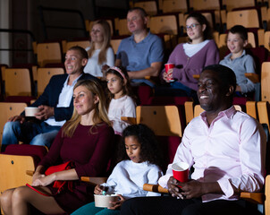 caucasian mother, african father and their children sitting at comedy in auditorium