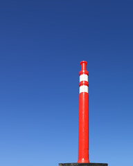 Single red and white traffic pylon under blue sky