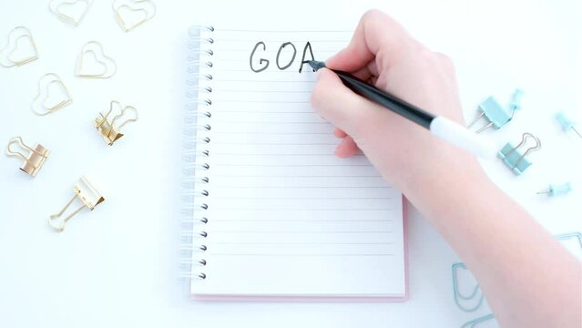 Female hand writes goals in a notebook on white background close-up.