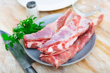 Fototapeta premium Fresh uncooked pork ribs on ceramic plate with parsley and kitchen knife. Ingredient for cook