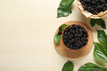 Fototapeta na wymiar Wicker basket of delicious ripe black mulberries on white table, flat lay. Space for text