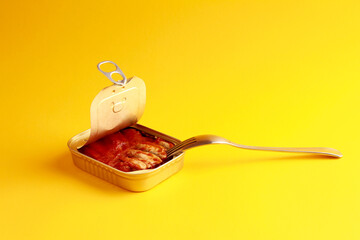 Canned fish sprats in tomato sauce in open tin can with easy openable lid with fork on a yellow...