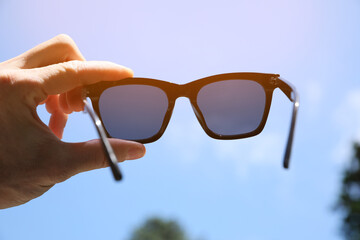 Mature man holding stylish sunglasses outdoors on sunny day, closeup